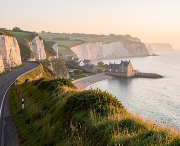 Route côtière normande longeant de hautes falaises blanches, avec un village portuaire et une campagne verdoyante baignés par la lumière dorée du lever du soleil.